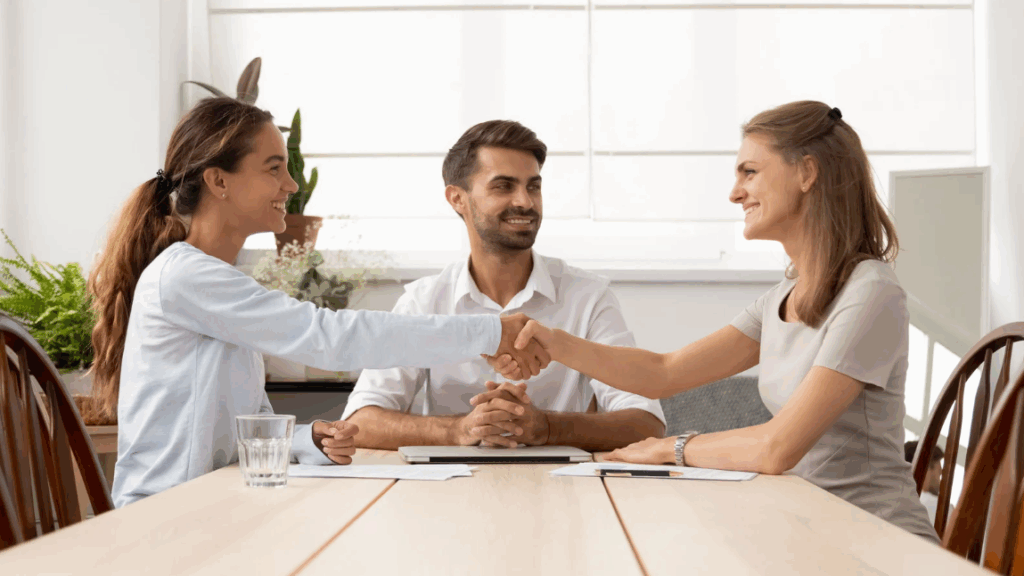 Deux collègues se serrent la main devant un manager, symbolisant la résolution d’un malentendu au travail et le retour à une communication apaisée en équipe.